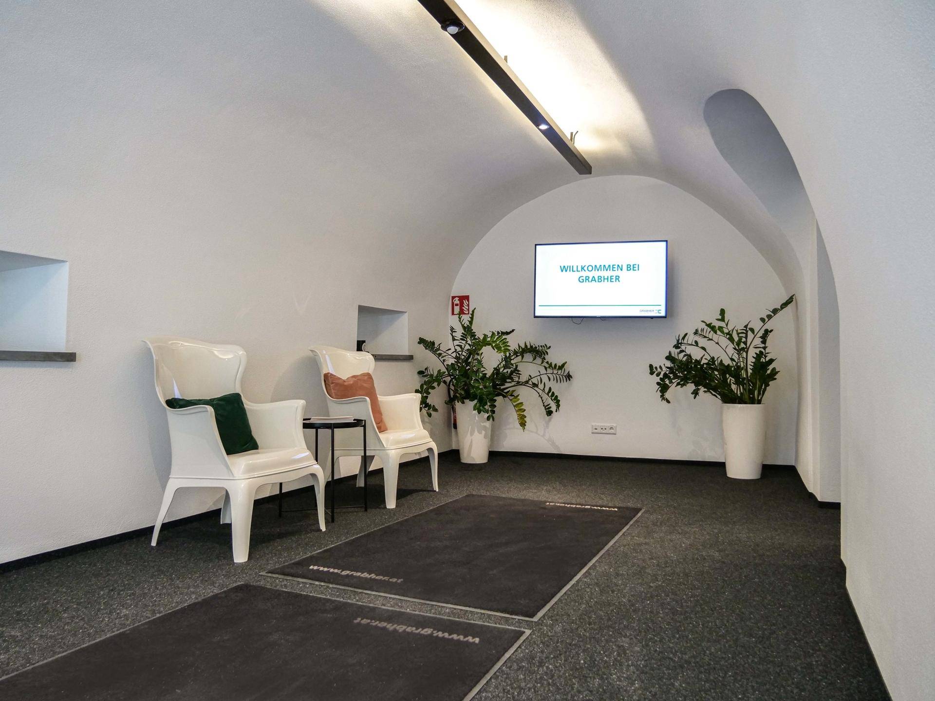 Empfangsbereich mit gewölbter Decke, modernen Sitzgelegenheiten und einem Informationsbildschirm.