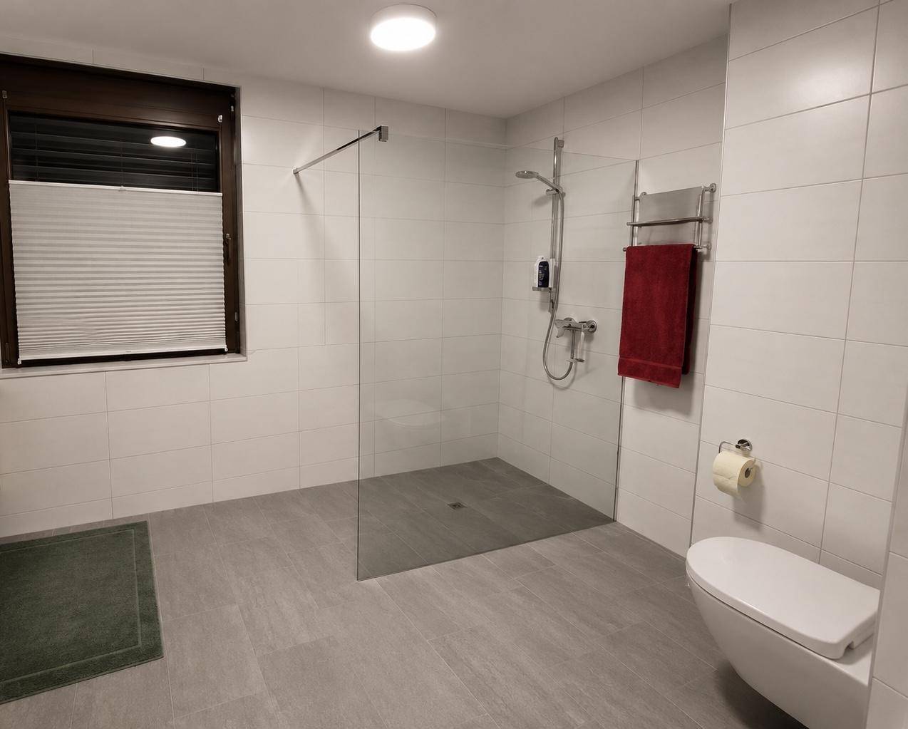 Modernes Badezimmer mit bodengleicher Dusche, Wand-WC und hellen Fliesen.