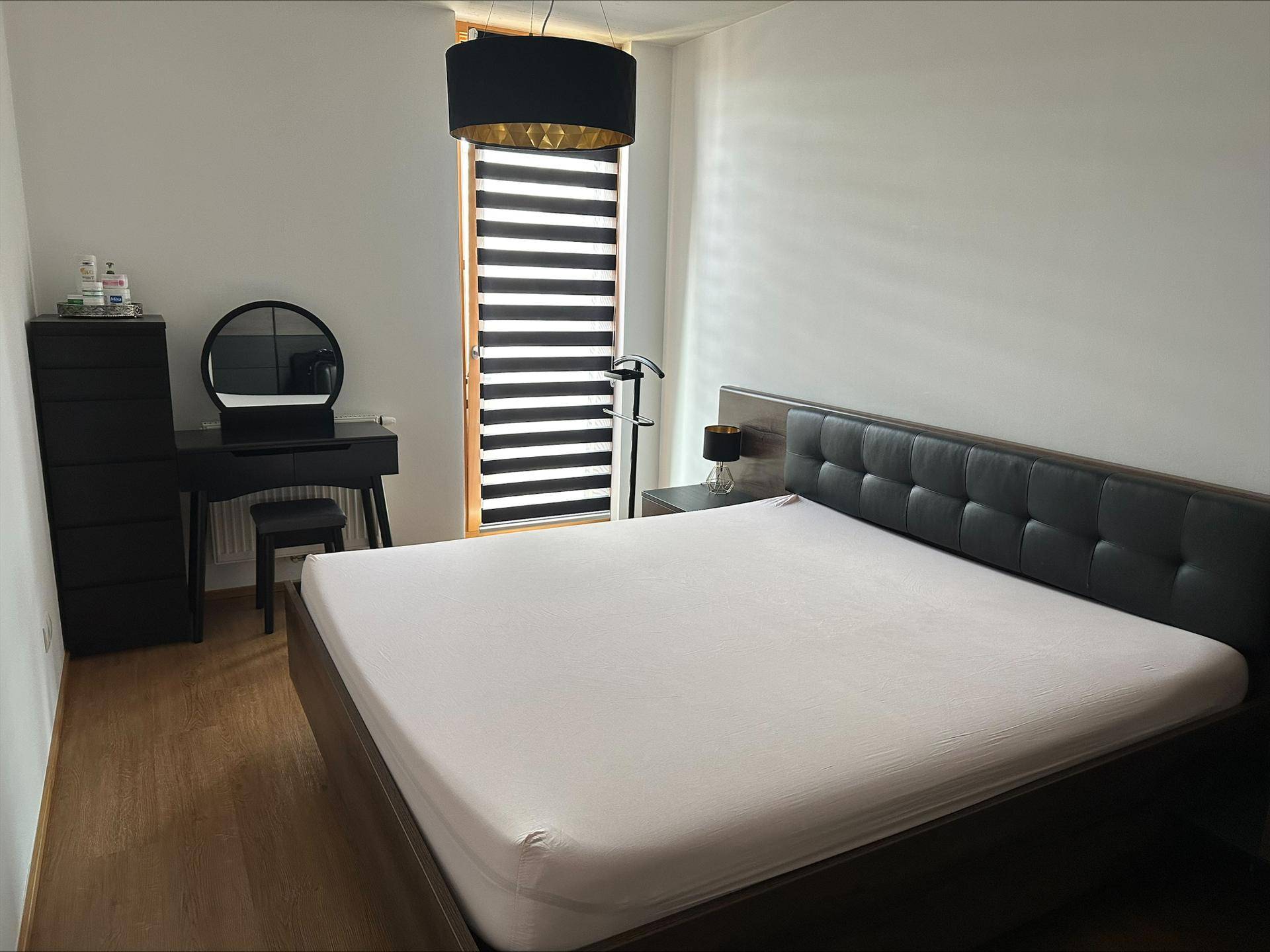 Helles Schlafzimmer mit Doppelbett, dunklem Kopfteil und einem modernen Schminktisch am Fenster.