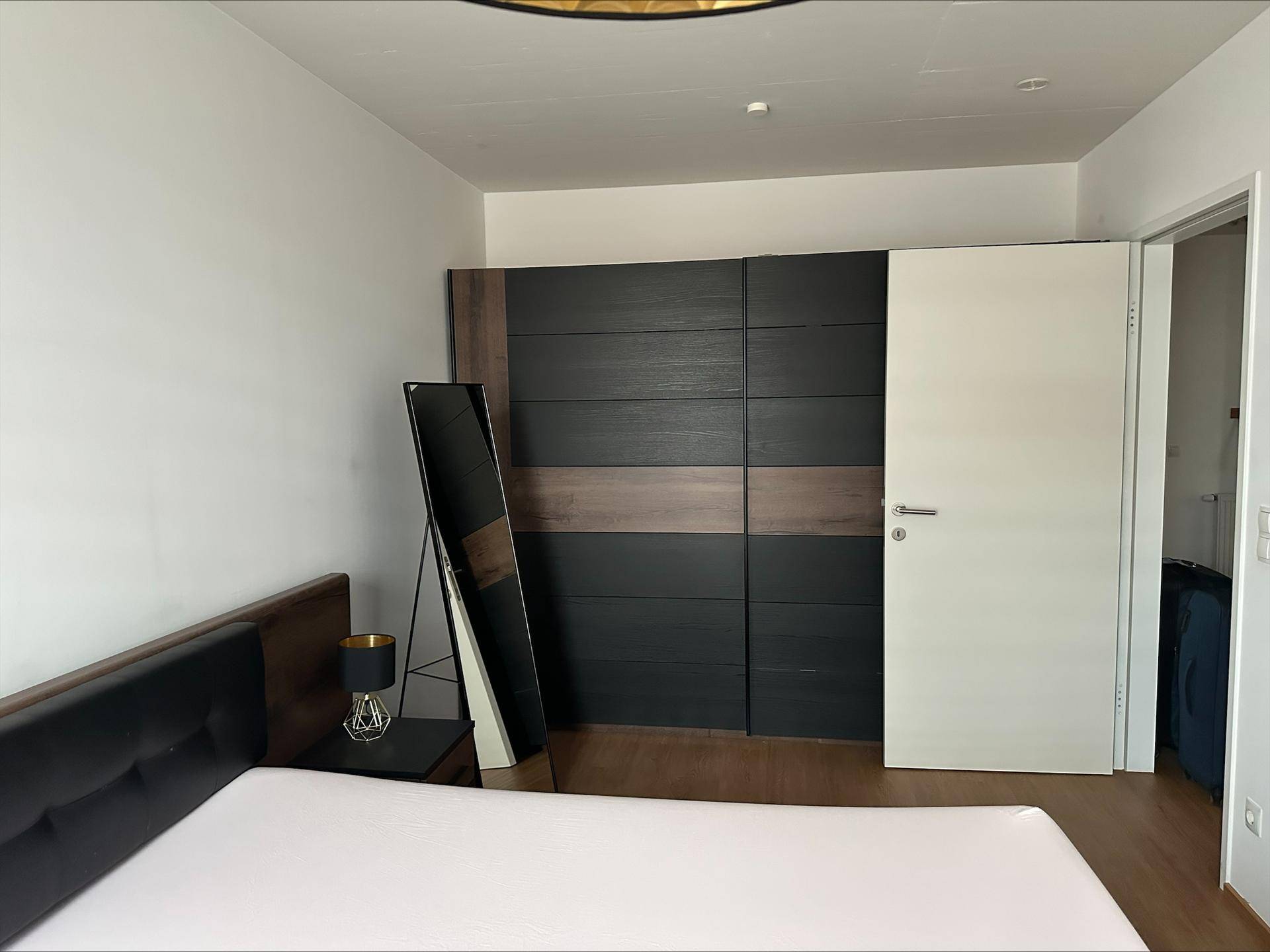 Schlafzimmer mit großem Kleiderschrank in Holz- und Anthrazitoptik und einem Ganzkörperspiegel.