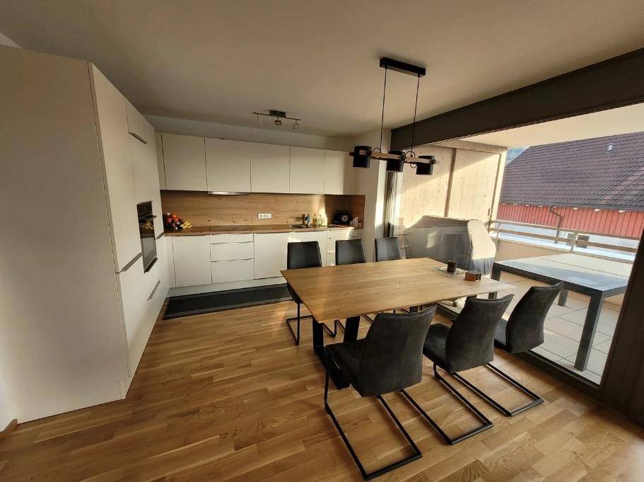 Moderne Einbauküche mit Essbereich, Holzakzenten und direktem Zugang zum sonnigen Balkon.