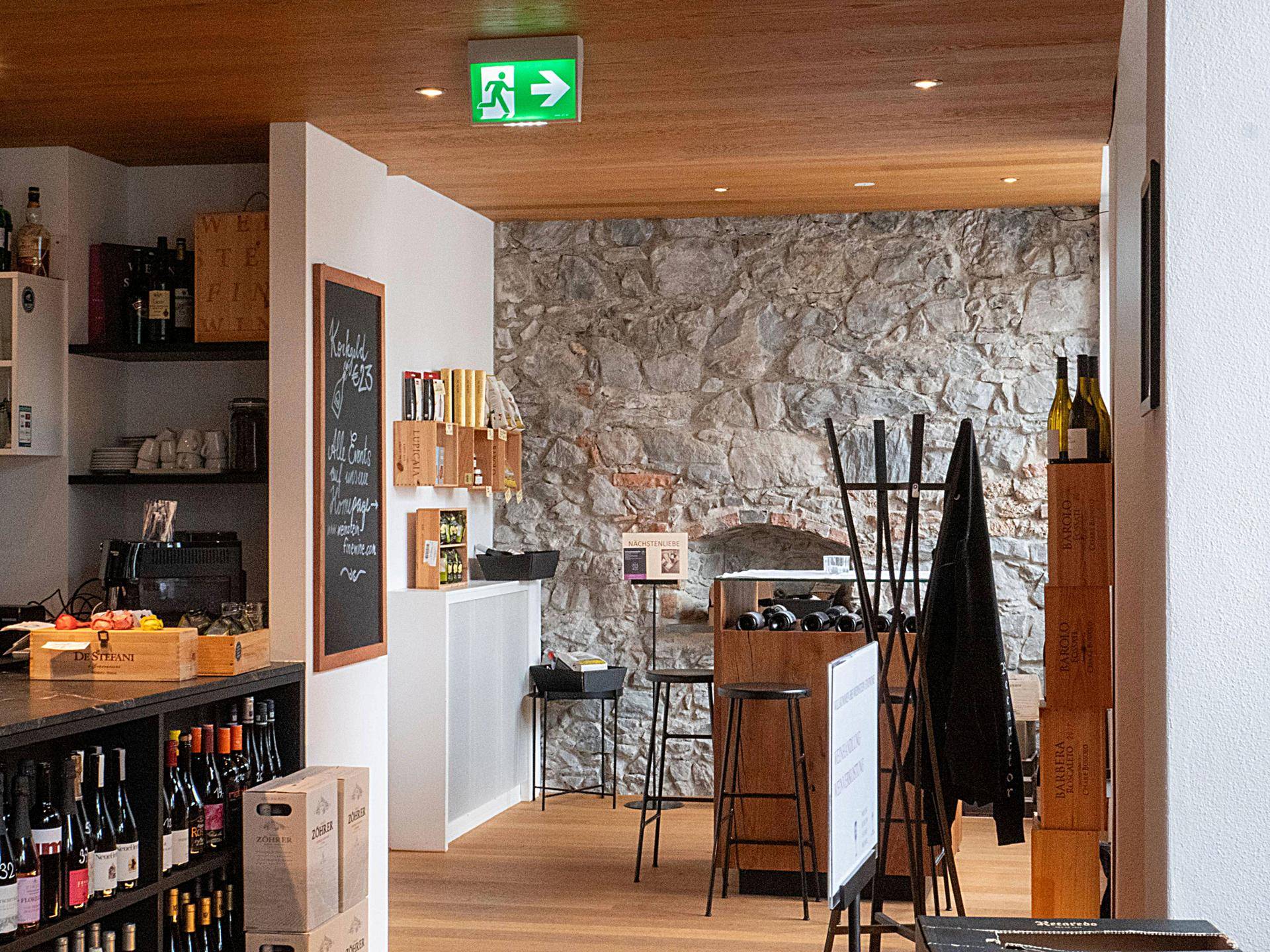 Innenansicht eines Weinladens mit Holzboden, Steinwand und Weinflaschenregalen.