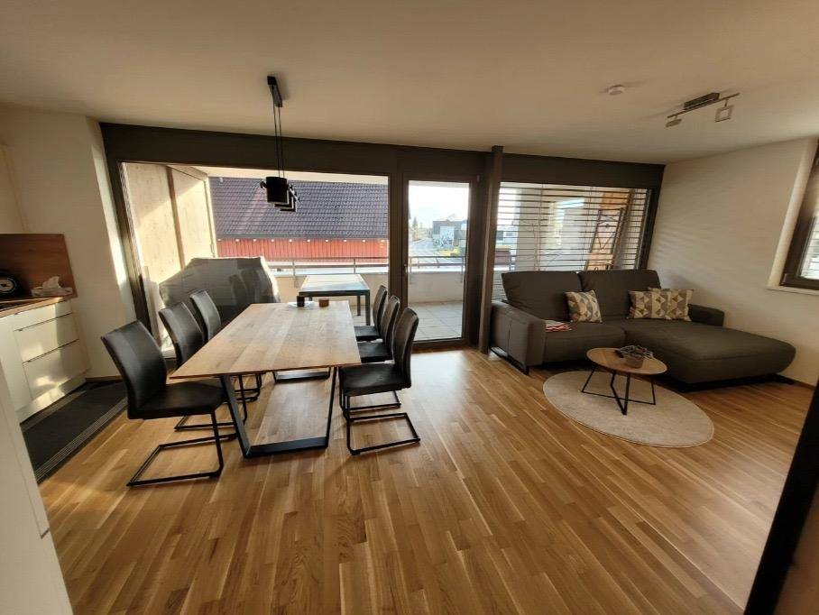 Lichtdurchfluteter Wohn-Essbereich mit Holzboden, gemütlichem Sofa und Zugang zum Außenbereich.