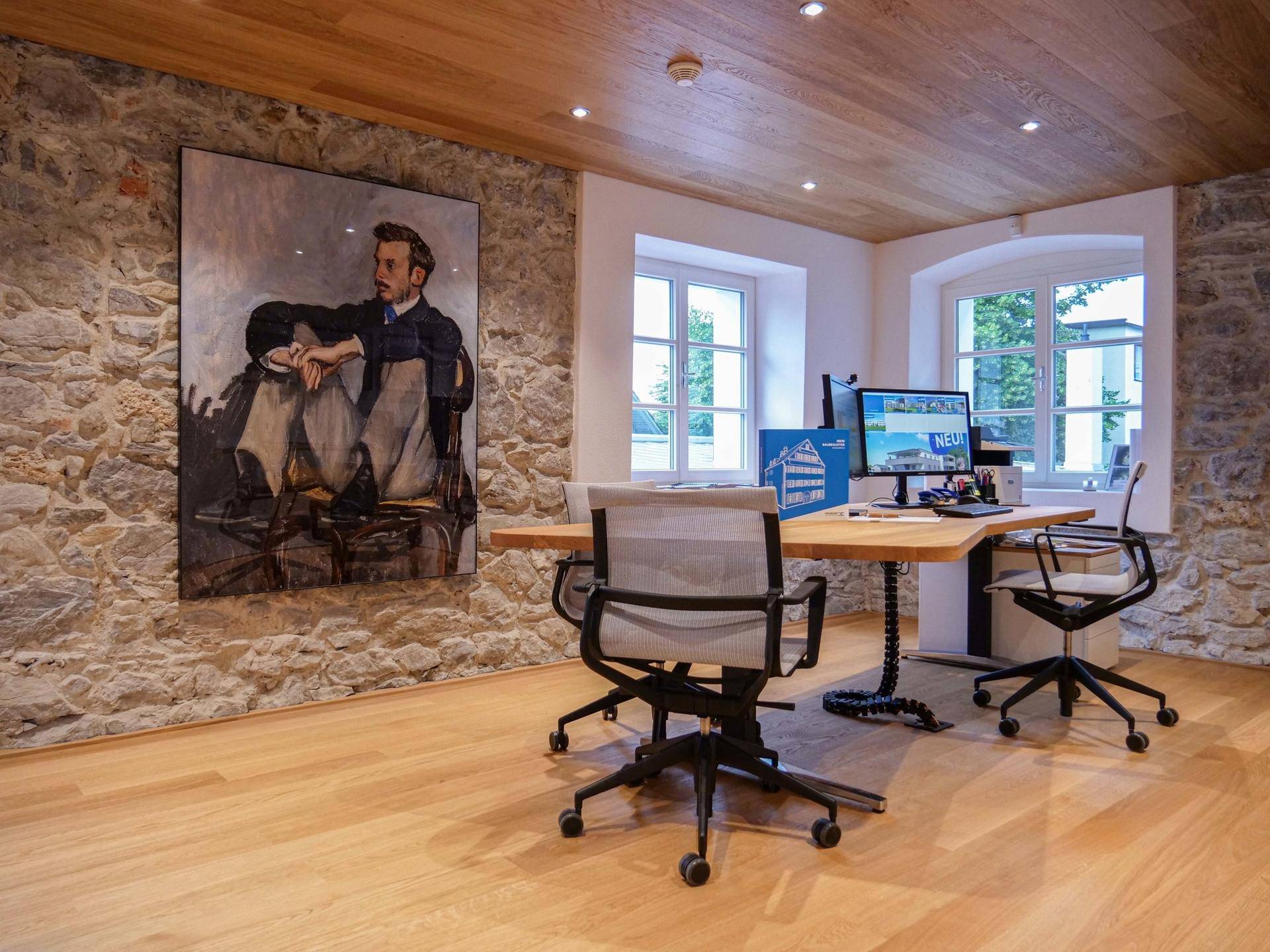 Helles Büro mit Holzboden, freigelegter Steinwand und großen Fenstern mit Ausblick.