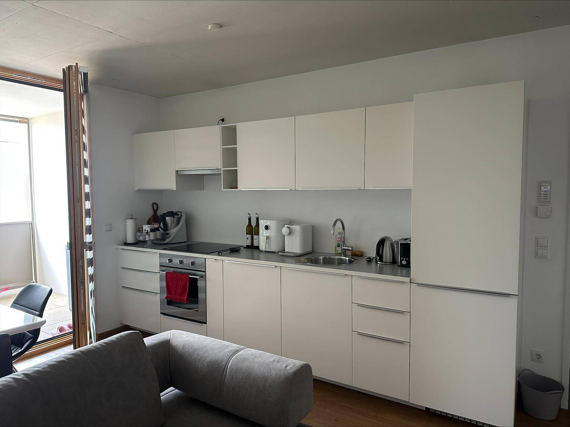 Moderne weiße Einbauküche mit integrierten Geräten und Zugang zu einem Balkon oder einer Loggia.
