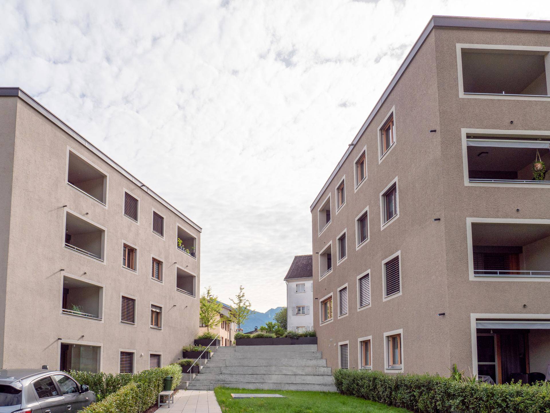 Blick zwischen zwei modernen Gebäuden mit beigen Fassaden und Loggien, mit Treppen und Grünflächen dazwischen.