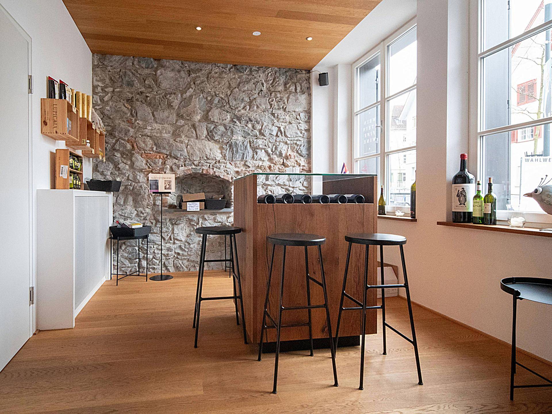 Heller Verkaufsraum mit großen Fenstern, Holzboden und einer zentralen Weinpräsentationstheke.