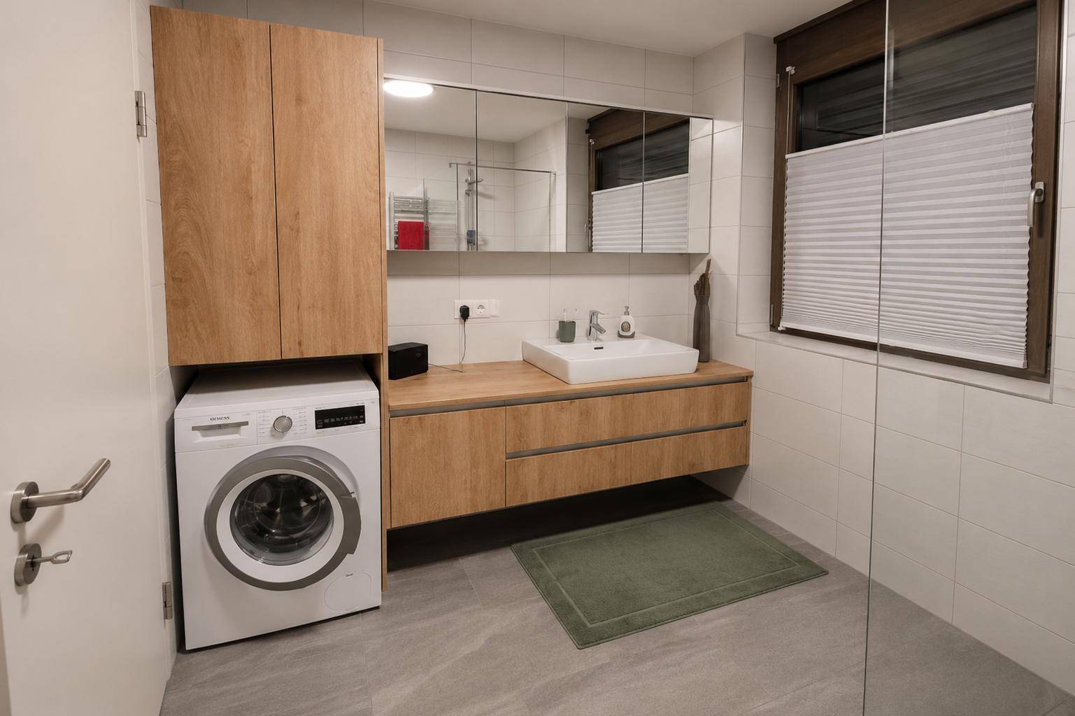 Funktionales Badezimmer mit Waschmaschine, Holzwaschtisch und Spiegelschrank, hell gefliest.