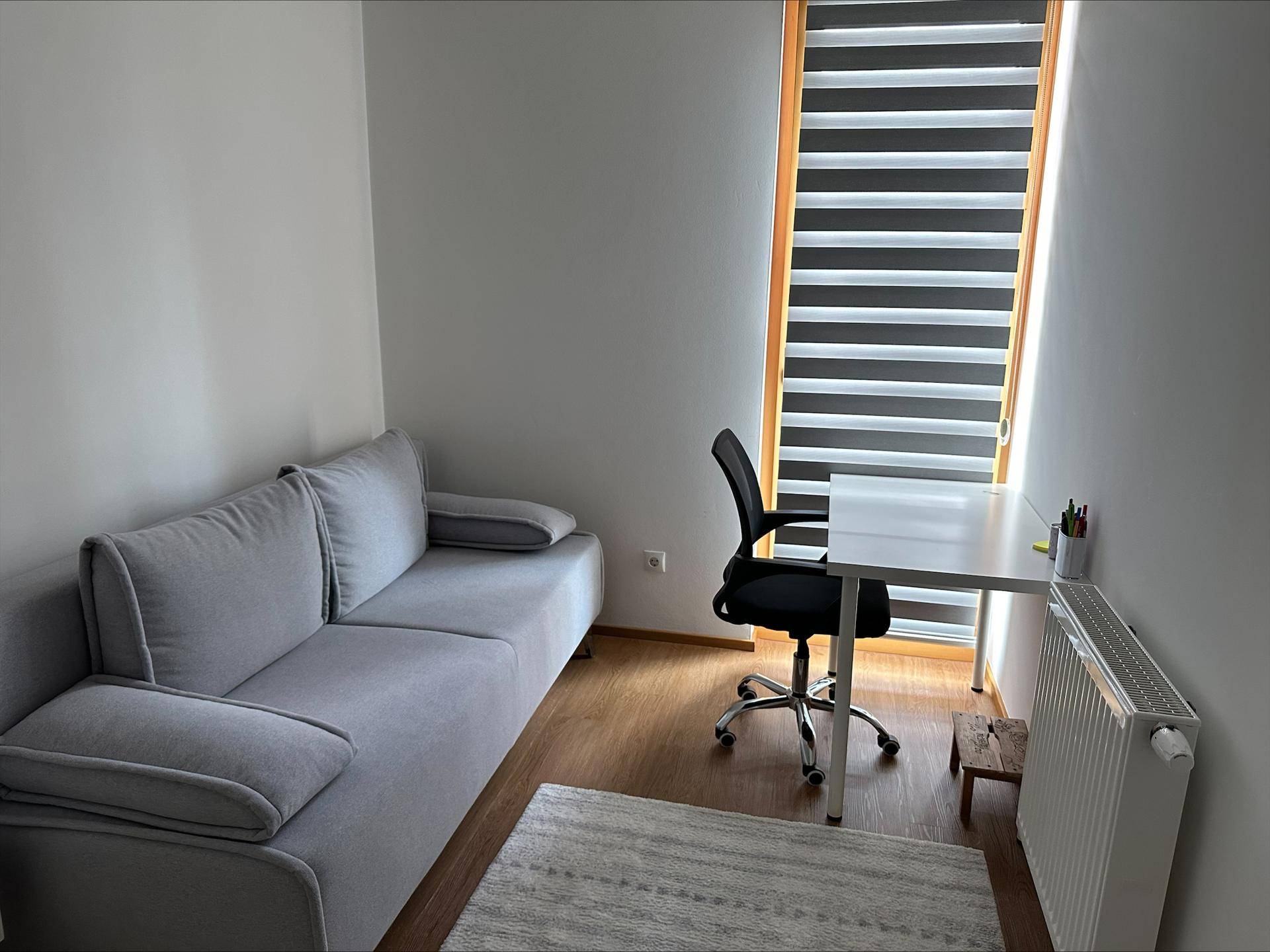 Kleines Arbeitszimmer mit Sofa, Schreibtisch und Bürostuhl, ideal für Home-Office-Tätigkeiten.