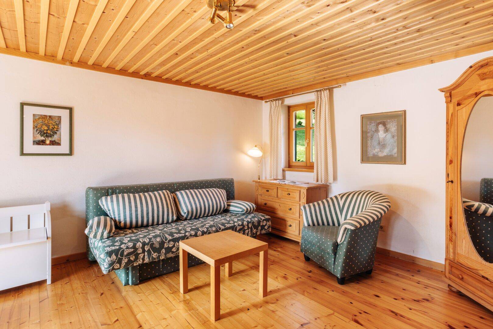 Wohn- oder Gästezimmer mit Schlafsofa, Holzmöbeln und einer Holzlamellendecke.