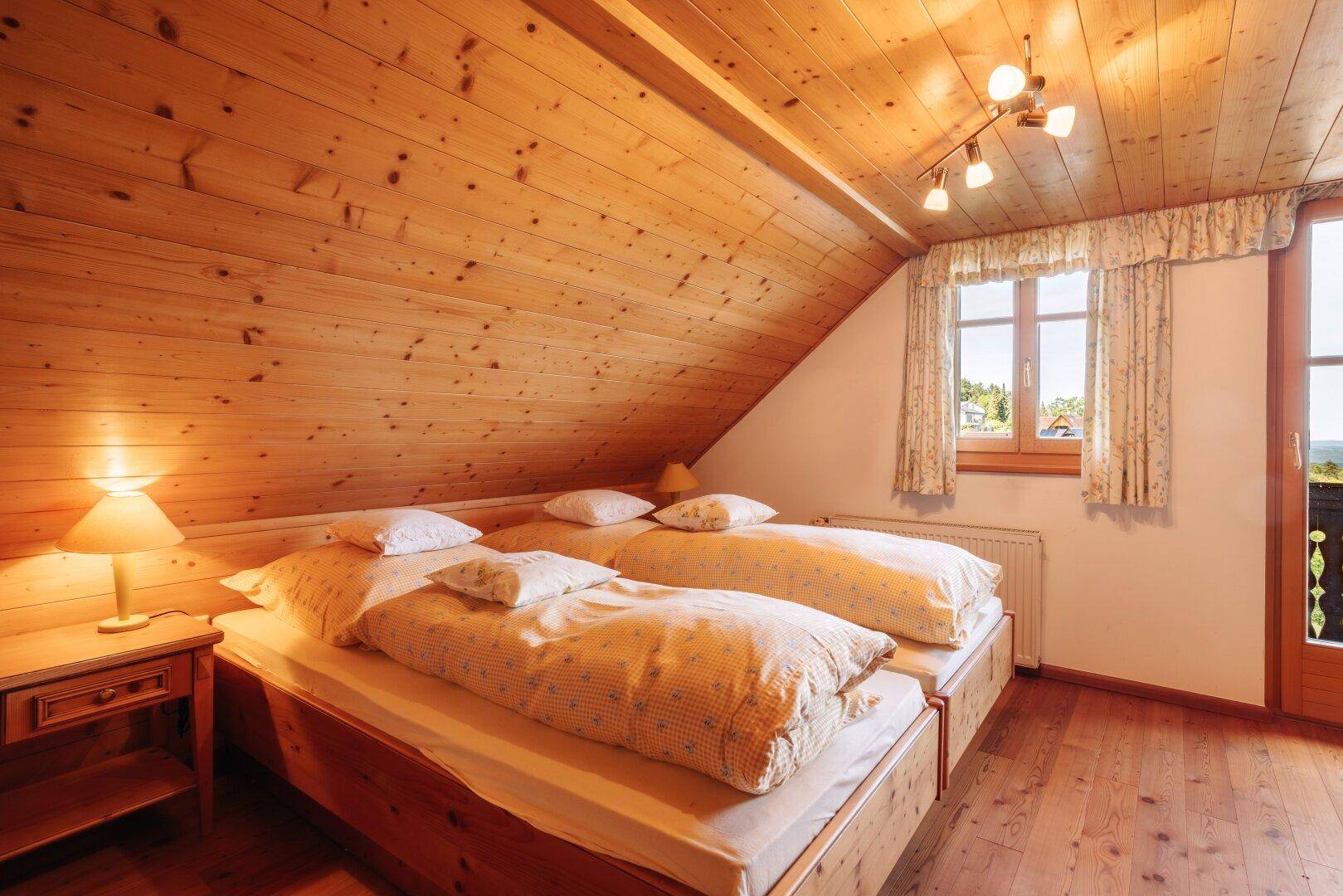 Schlafzimmer mit zwei Einzelbetten, schräger Holzdecke und Fenster mit schöner Aussicht.