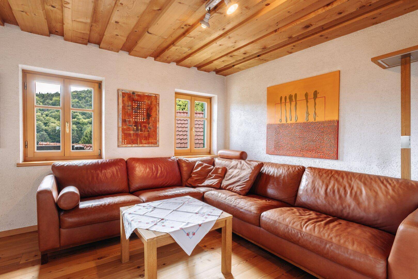Wohnzimmer mit großem braunem Ledersofa, Holzdecke und modernen Kunstwerken an den Wänden.