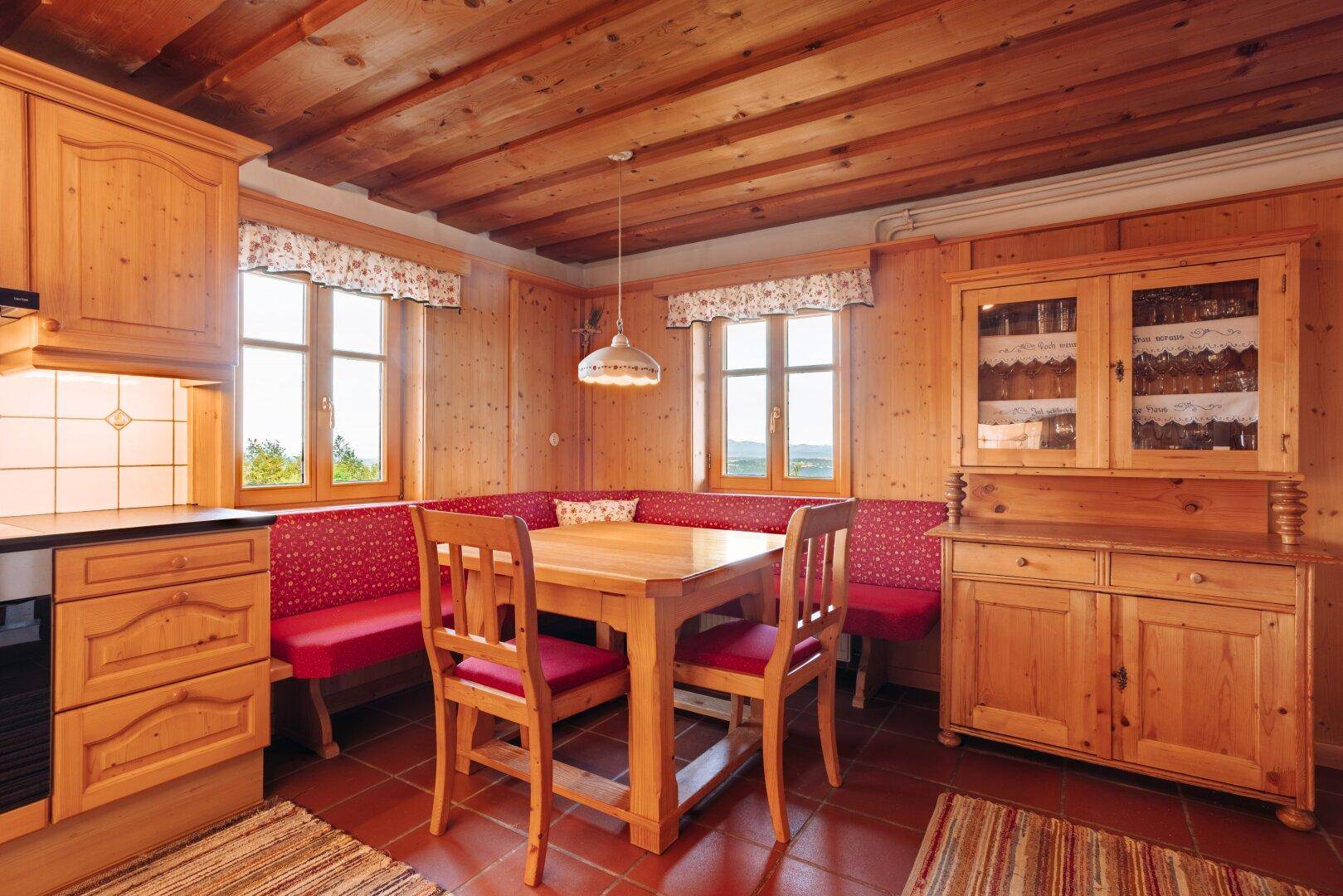 Gemütliche Wohnküche mit Holzmöbeln, roten Sitzbänken und Terrakottafliesenboden.
