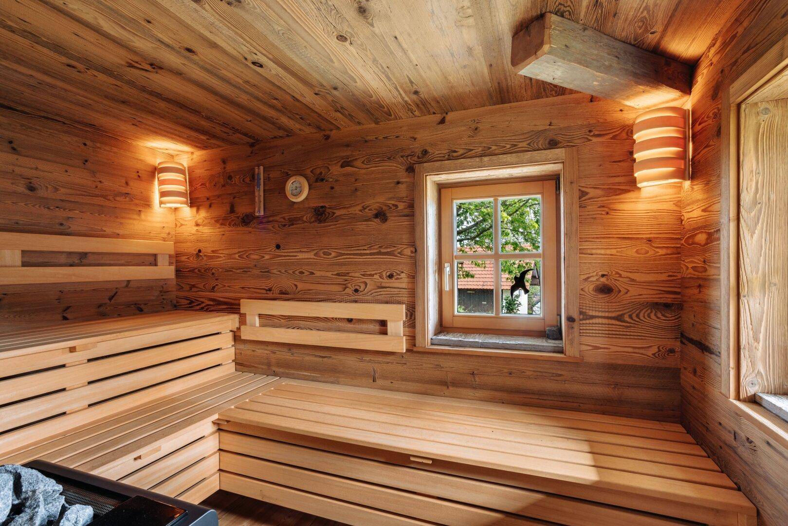 Gemütliche Holzsauna mit Sitzbänken und einem kleinen Fenster, das Tageslicht hereinlässt.