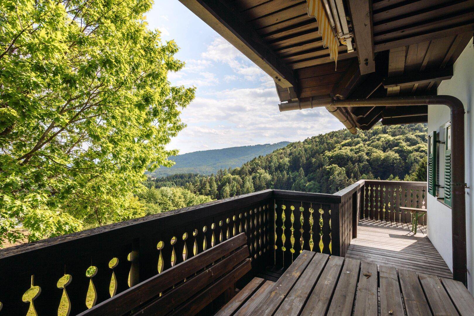 Geräumiger Holzbalkon mit Sitzgelegenheiten und atemberaubendem Panoramablick auf bewaldete Hügel.