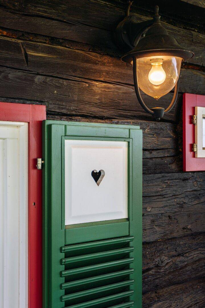 Traditionelle Außenlampe über einem grünen Fensterladen mit Herzmotiv an einer Holzwand.
