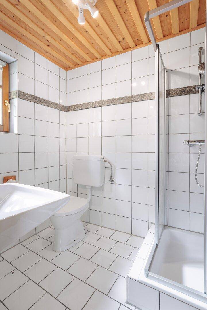 Badezimmer mit weißen Fliesen, Toilette und einer modernen Duschkabine.