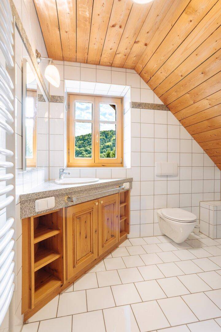 Badezimmer mit weißen Fliesen, Holzdecke, Waschtisch mit Steinarbeitsplatte und Handtuchheizkörper.
