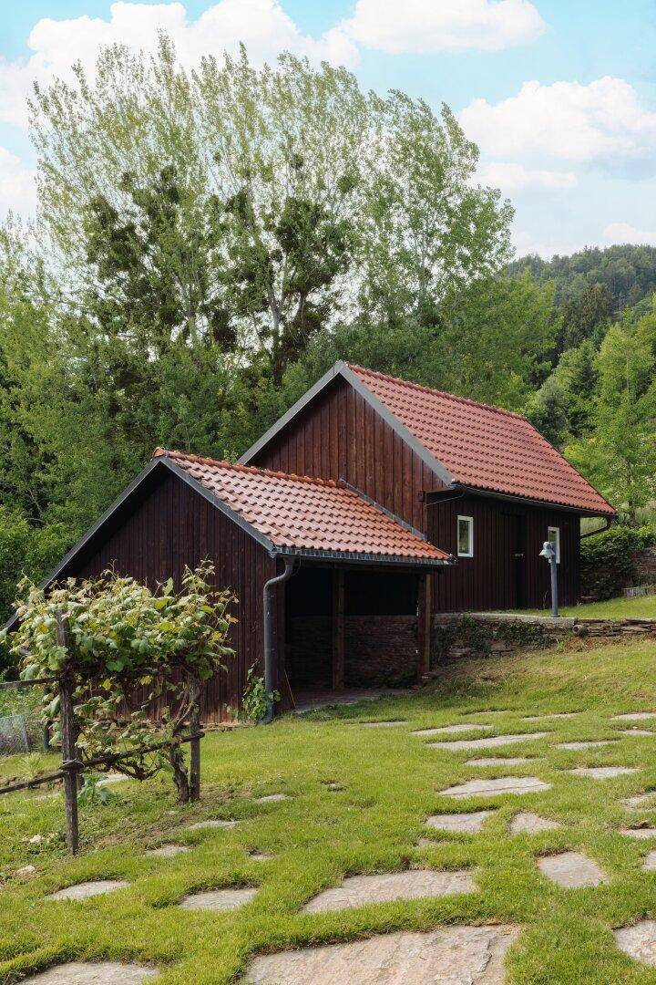 Kleines Holzgebäude mit rotem Ziegeldach und umgebender grüner Wiese.
