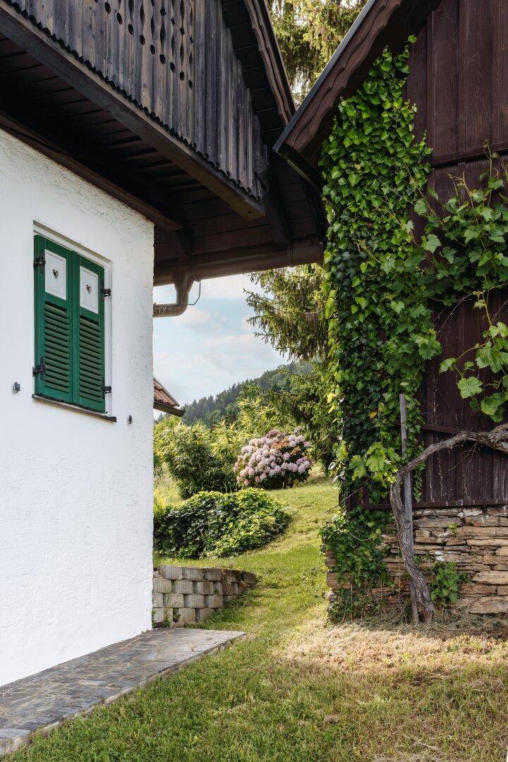 Seitenansicht eines Hauses mit Kletterpflanzen und einem grünen Gartenbereich im Hintergrund.