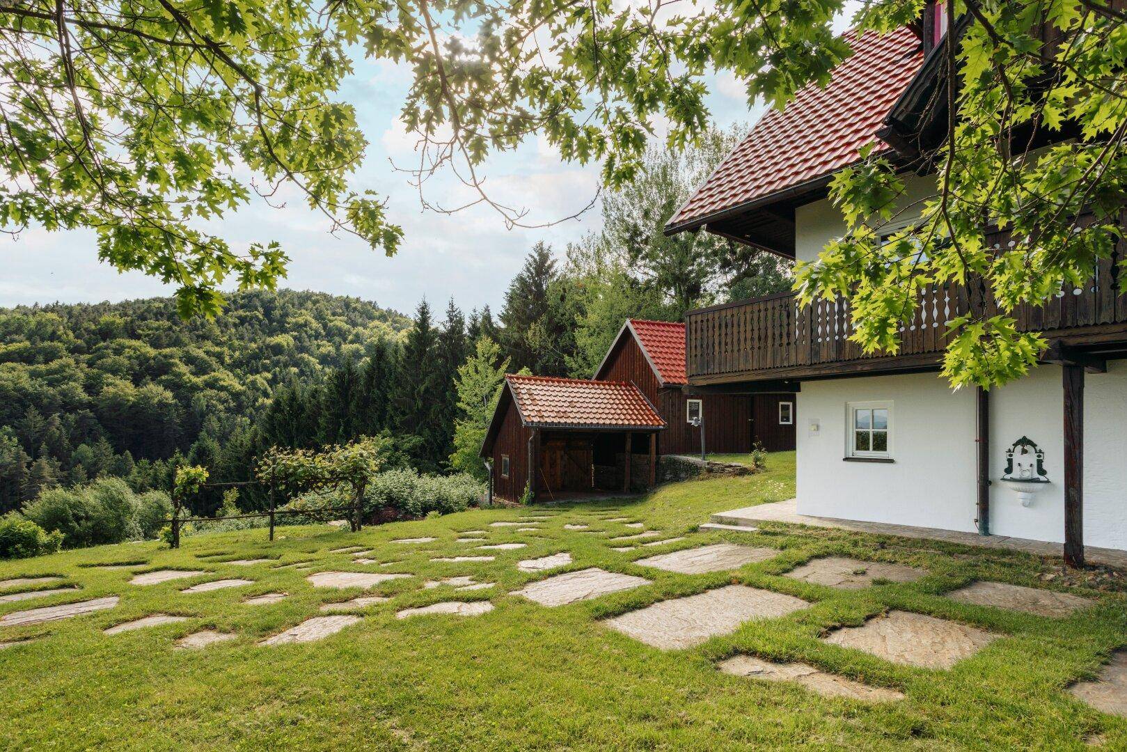 Gartenbereich neben dem Haus mit Steinplatten und einem malerischen Blick auf den umliegenden Wald.