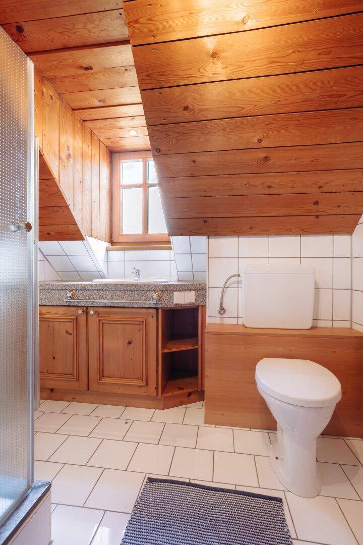 Badezimmer mit weißen Fliesen, Holzdecke, Toilette und Waschtisch mit Steinarbeitsplatte.