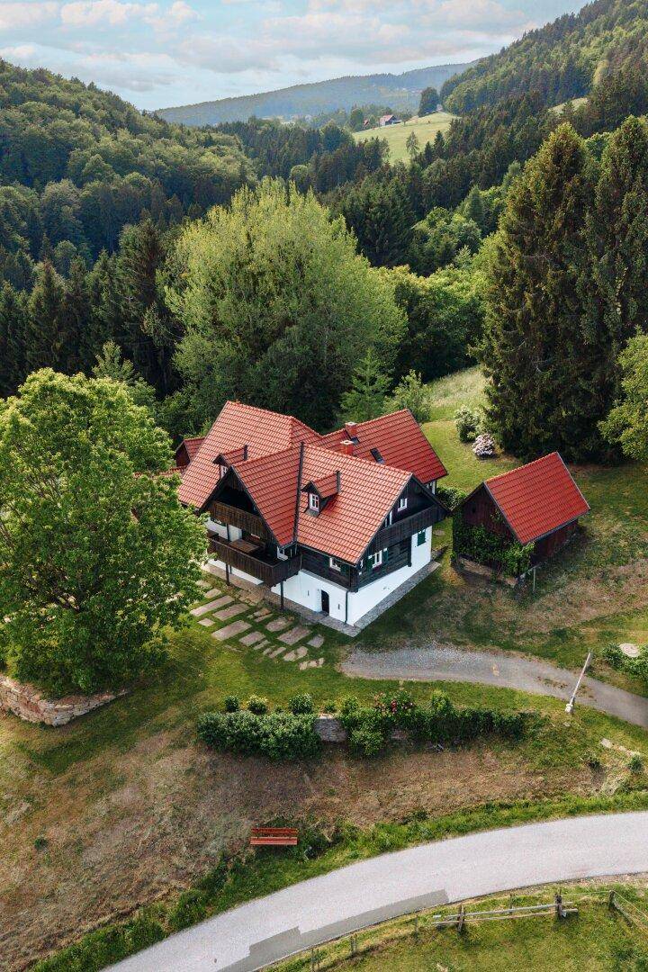 Luftaufnahme eines Hauses mit rotem Dach inmitten einer grünen, bewaldeten Landschaft.