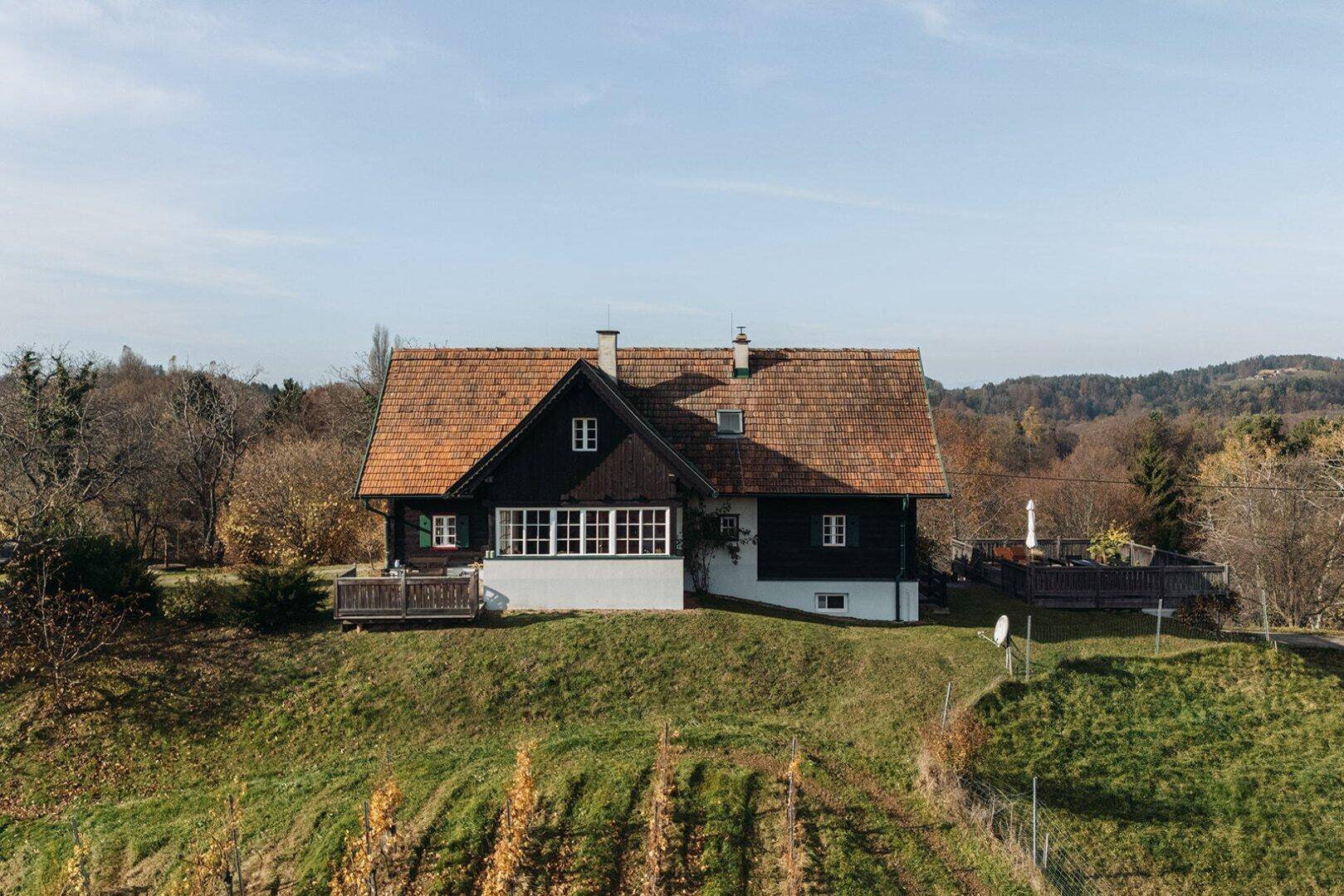 Traditionelles Landhaus mit Ziegeldach auf einem Hügel, umgeben von Natur und Weinbergen.