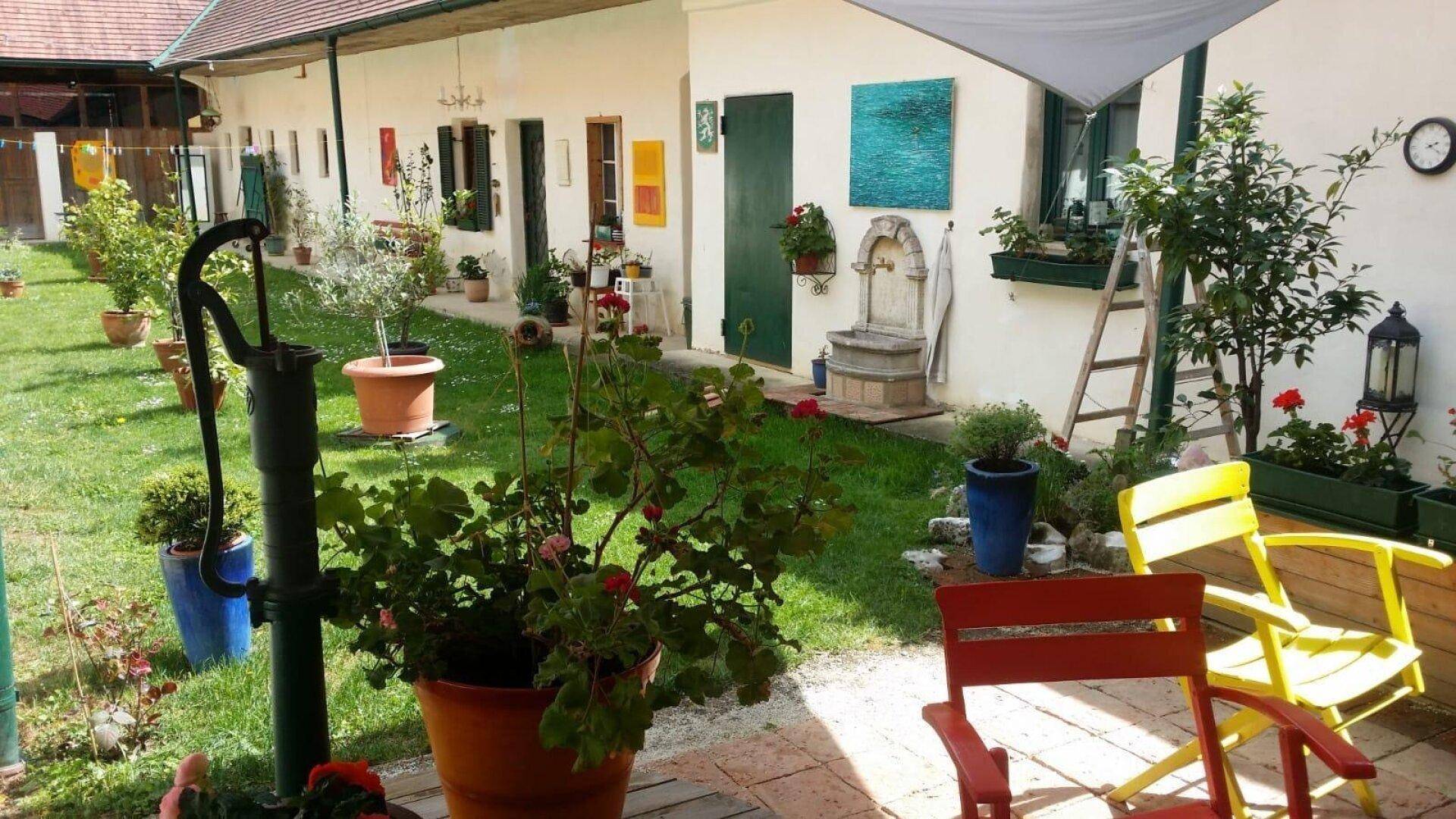 Gemütlicher Innenhof mit bunten Gartenstühlen, Pflanzen und einem historischen Wasserbrunnen.