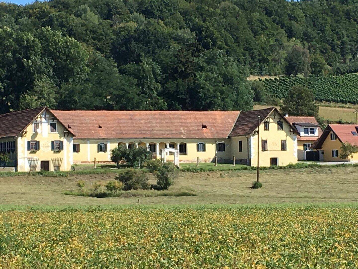 Historisches Gebäude in ländlicher Umgebung, umgeben von Feldern und bewaldeten Hügeln.