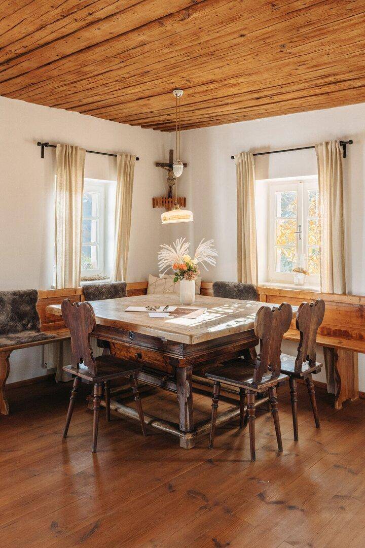 Rustikaler Essbereich mit Holztisch, Bänken und Stühlen unter einer Holzbalkendecke.