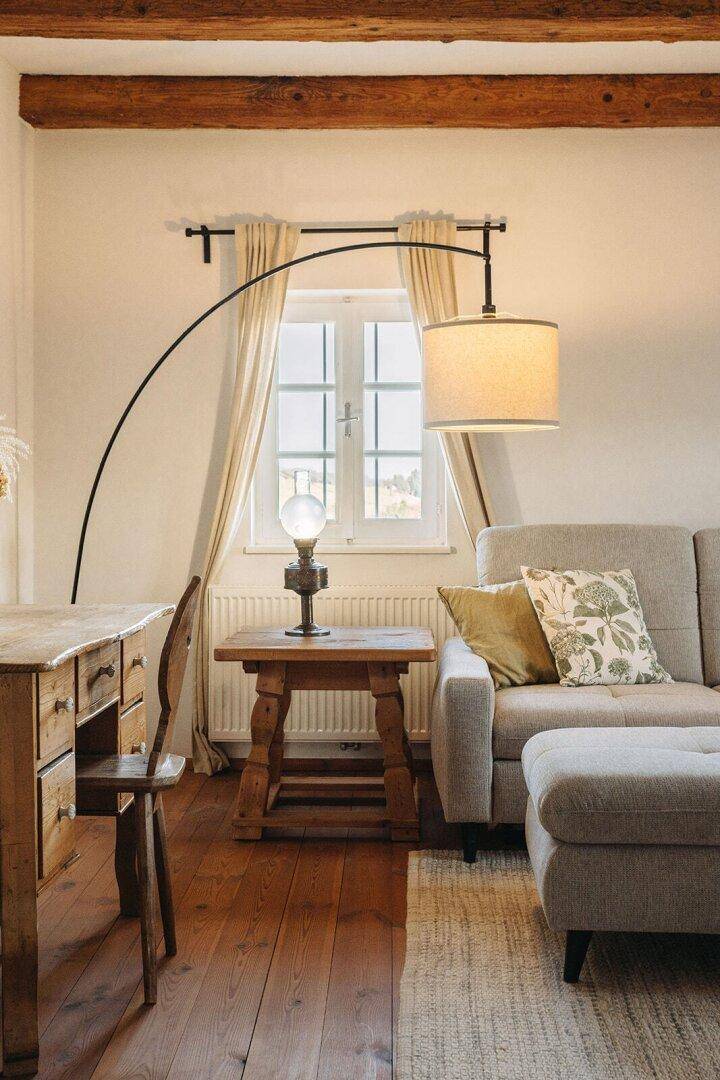 Heller Wohnbereich mit bequemem Sofa, Holzboden und einem Fenster mit Blick ins Grüne.