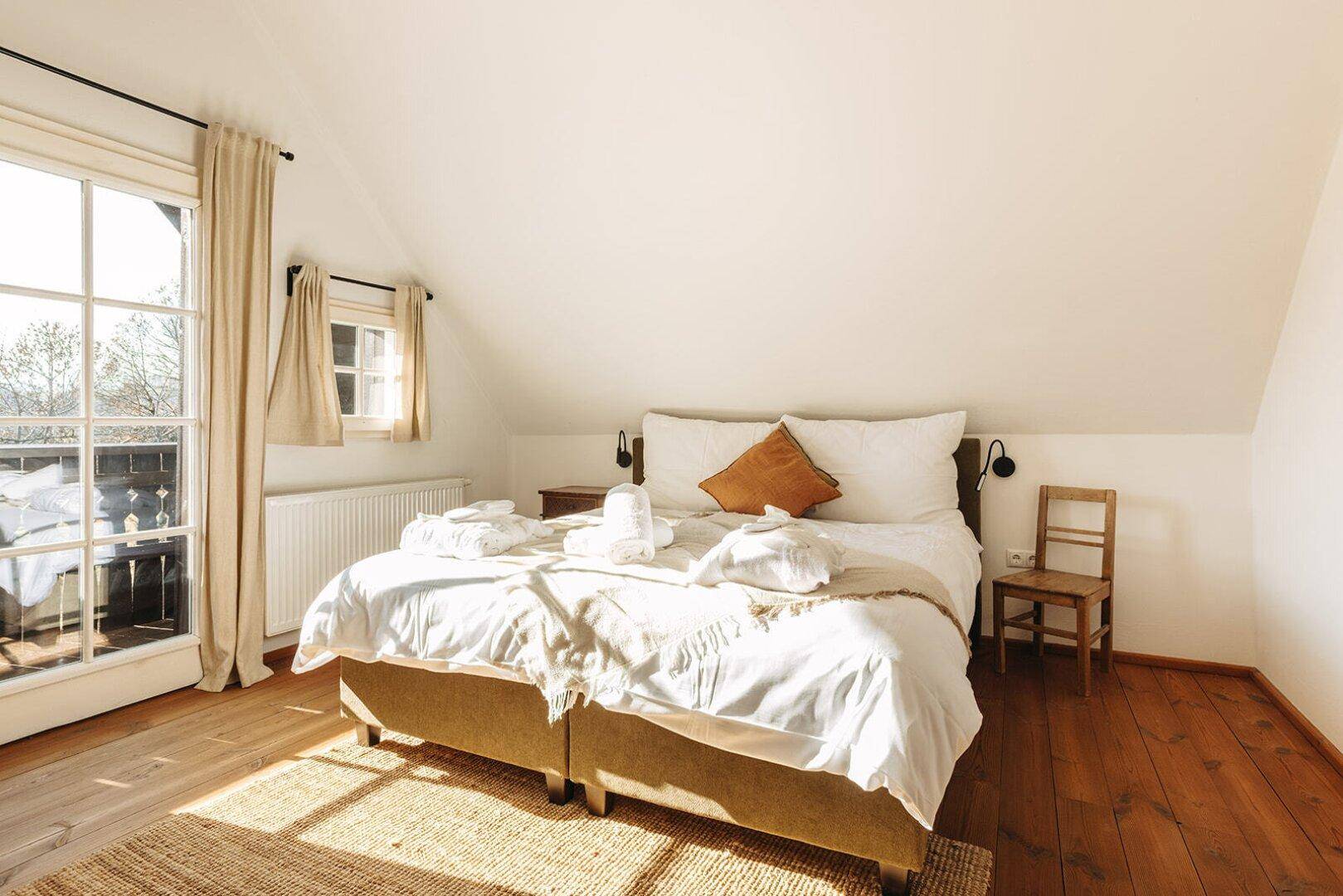 Helles Schlafzimmer mit Holzboden, Dachschräge und Zugang zu einem kleinen Balkon.