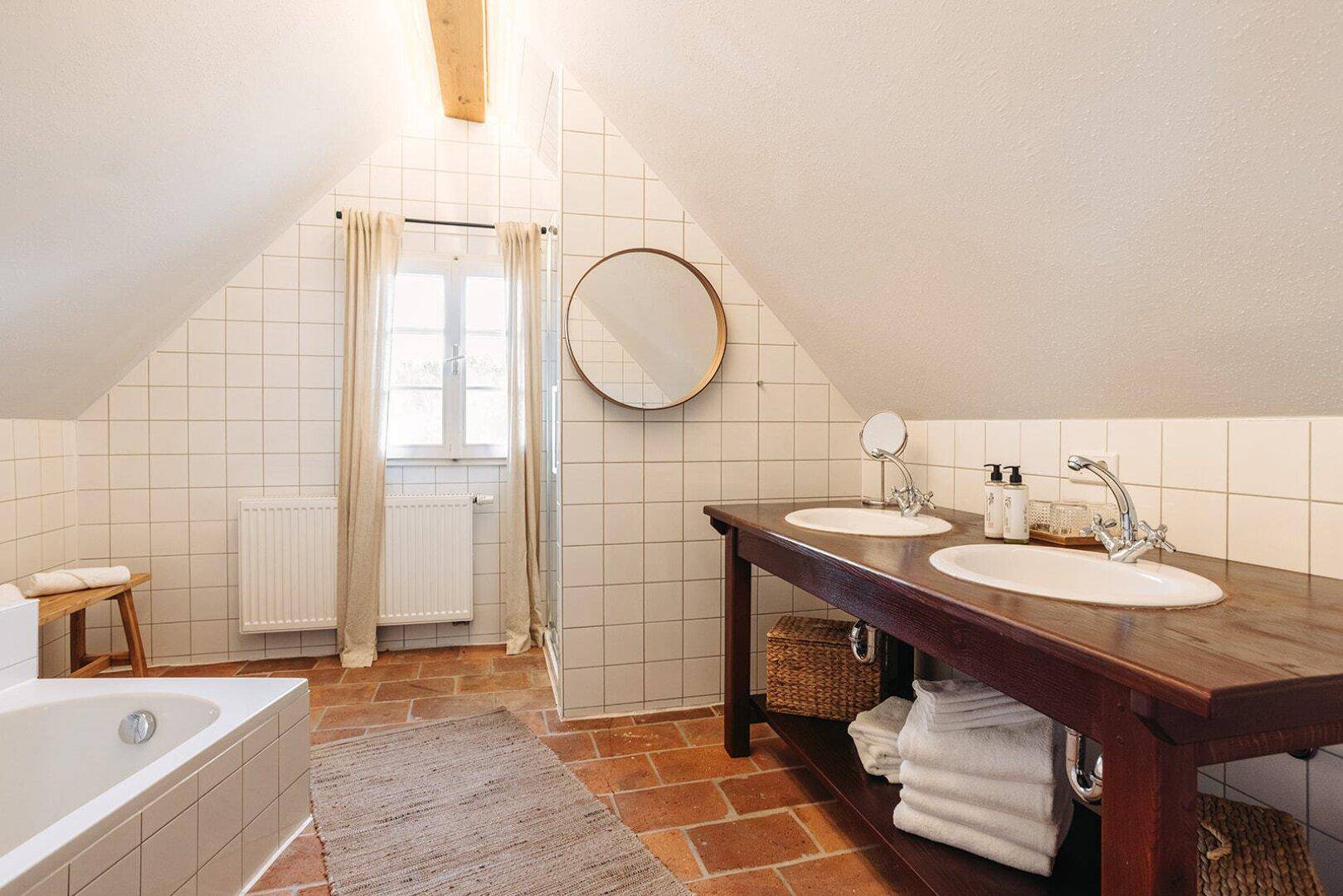 Geräumiges Badezimmer mit Doppelwaschbecken, Badewanne und weißen Fliesen unter Dachschräge.