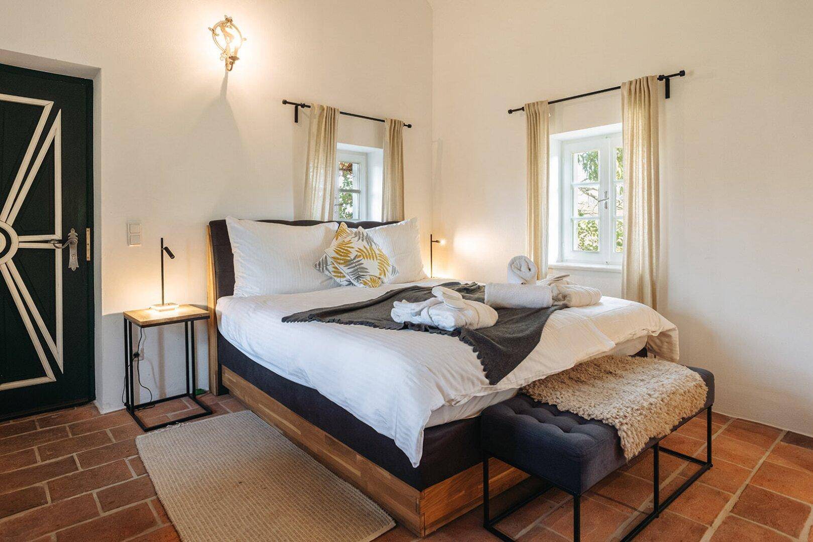 Gemütliches Schlafzimmer mit Terrakottaboden, traditioneller Tür und zwei Fenstern.
