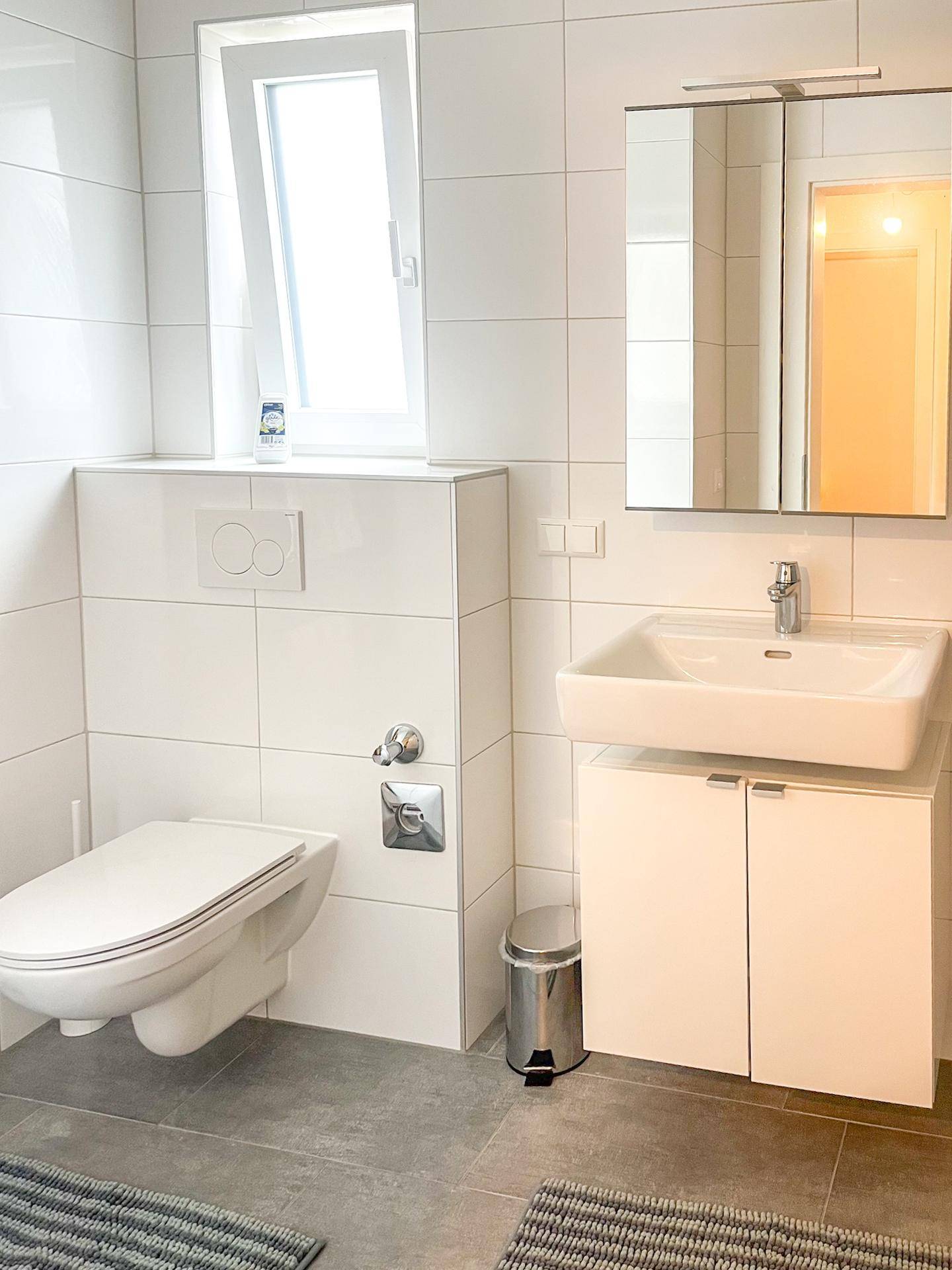 Modernes Badezimmer mit wandhängendem WC, Waschbeckenunterschrank und Fenster für Tageslicht.