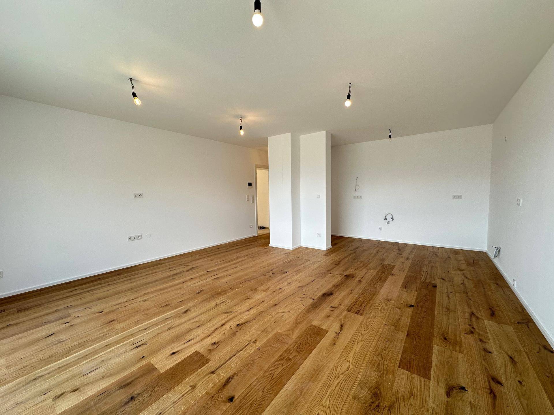 Großer, leerer Raum mit Holzboden und weißen Wänden, bereit für individuelle Gestaltung.