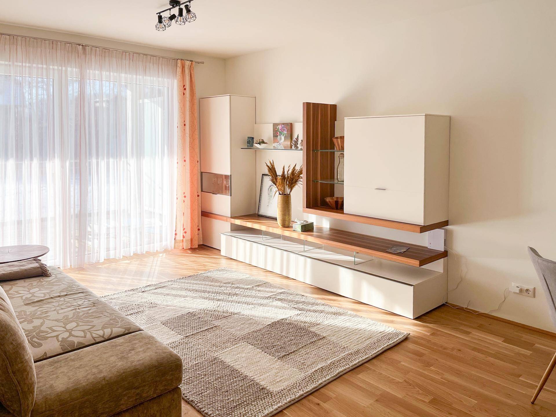 Lichtdurchflutetes Wohnzimmer mit Holzboden, beigem Sofa und moderner Wohnwand.