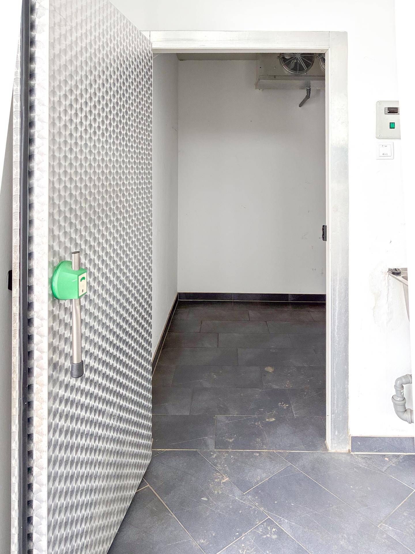 Offene Tür zu einem Kühlraum oder begehbaren Gefrierschrank mit einer markanten, strukturierten Metalltür.