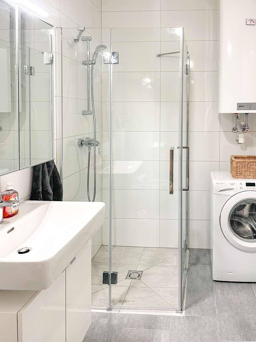 Badezimmer mit ebenerdiger Dusche, Waschbecken und integrierter Waschmaschine.