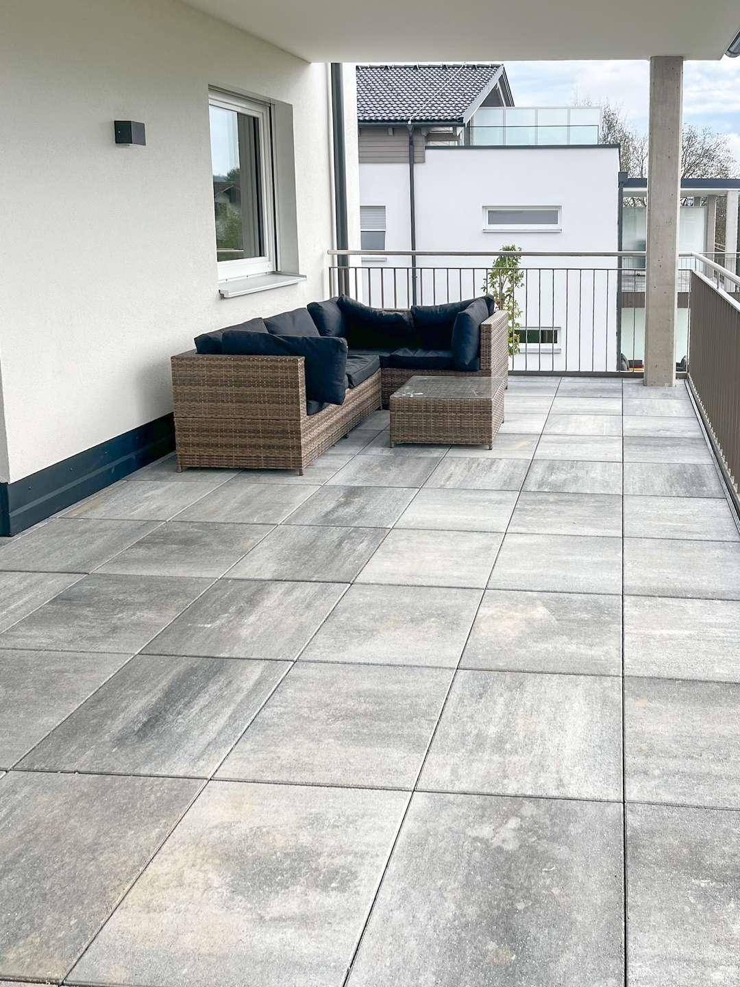 Moderner Balkon mit grauen Fliesen und gemütlicher Lounge-Ecke.