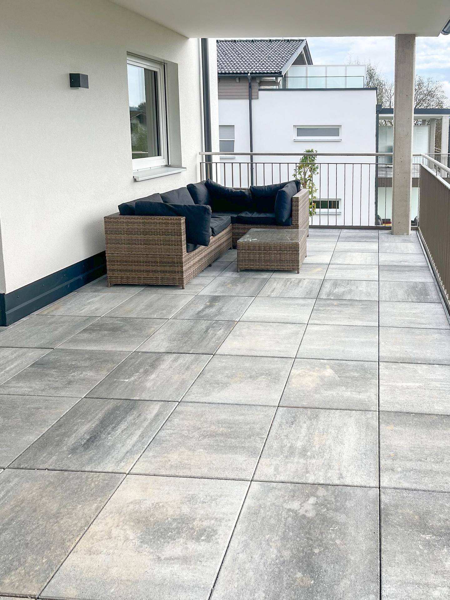 Moderne Terrasse mit grauen Fliesen und gemütlicher Lounge-Sitzgruppe am Gebäude.