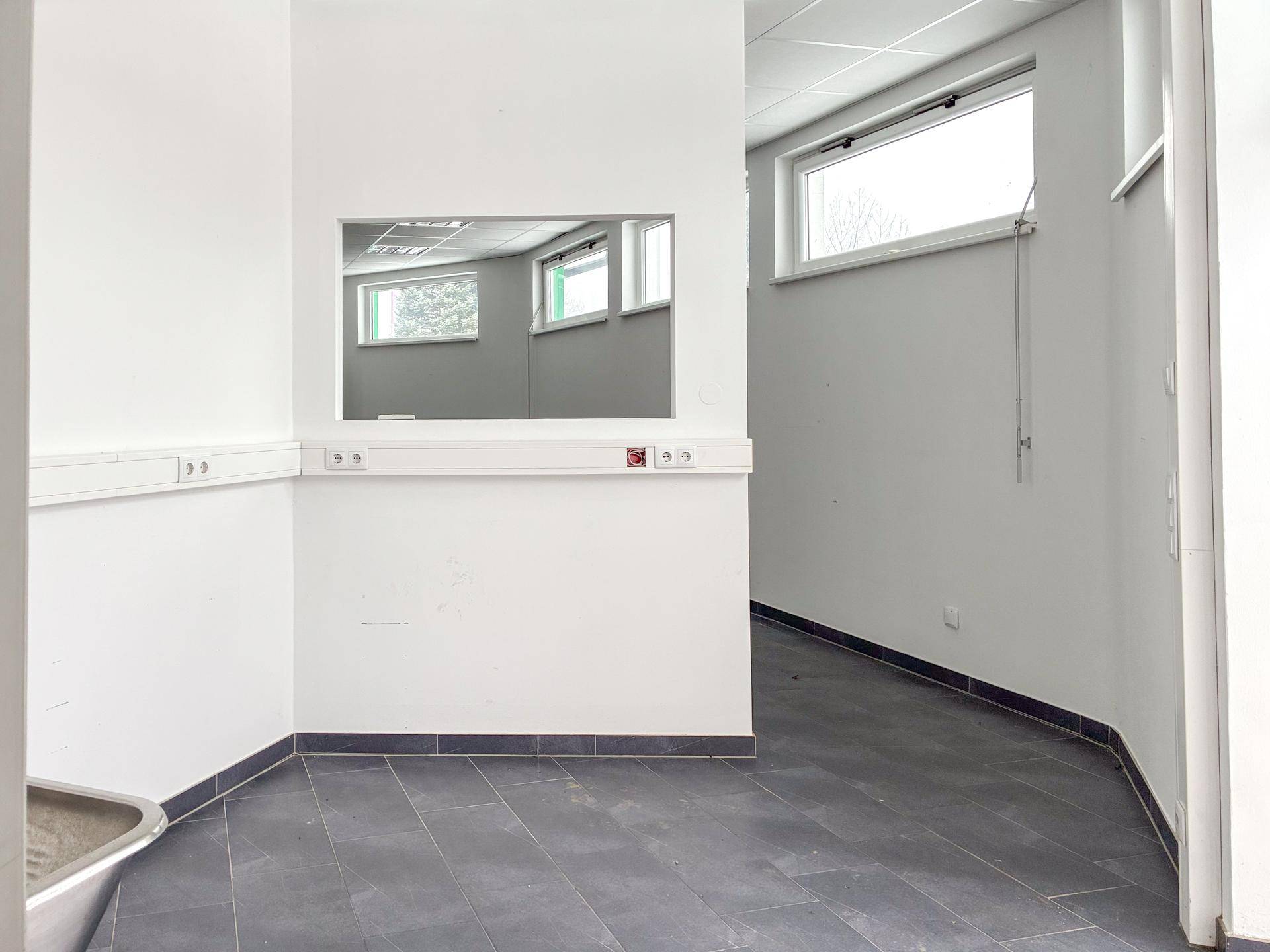 Kleinerer Raum innerhalb der Gewerbefläche mit einer praktischen Durchreiche und einem Fenster, ideal für ein Büro.