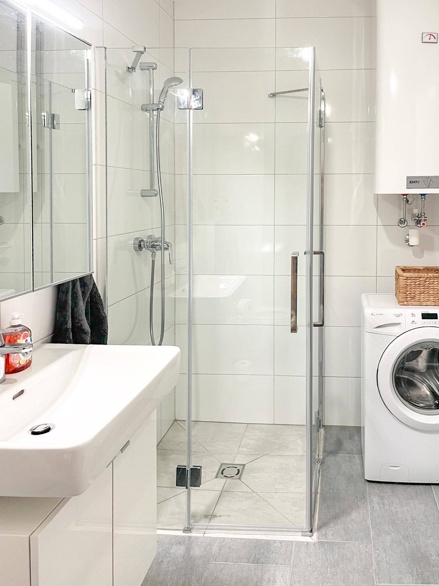 Helles Badezimmer mit moderner Glasdusche, Waschbecken und integrierter Waschmaschine.