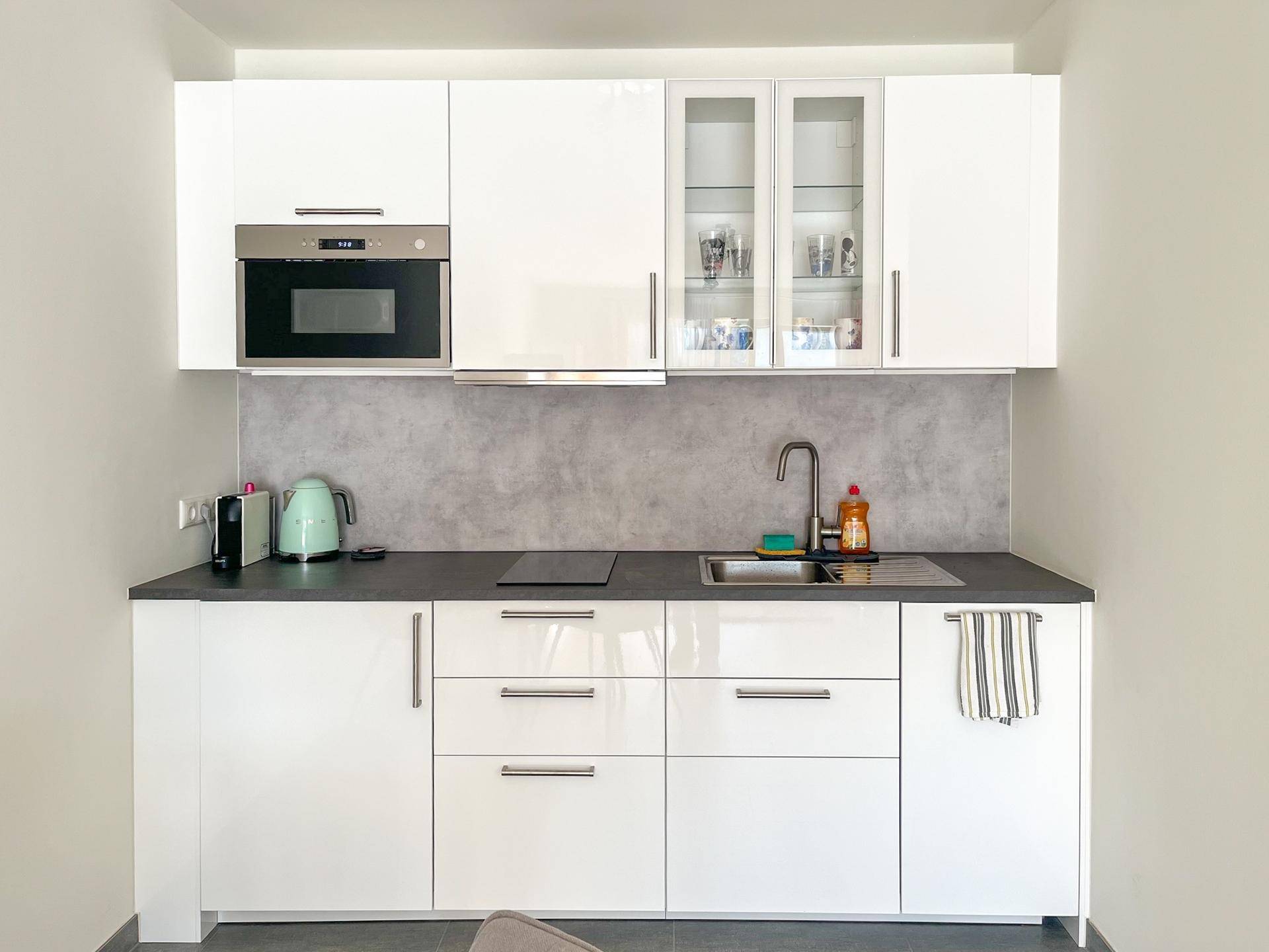 Moderne weiße Einbauküche mit Hochglanzfronten, integriertem Backofen und Induktionskochfeld.