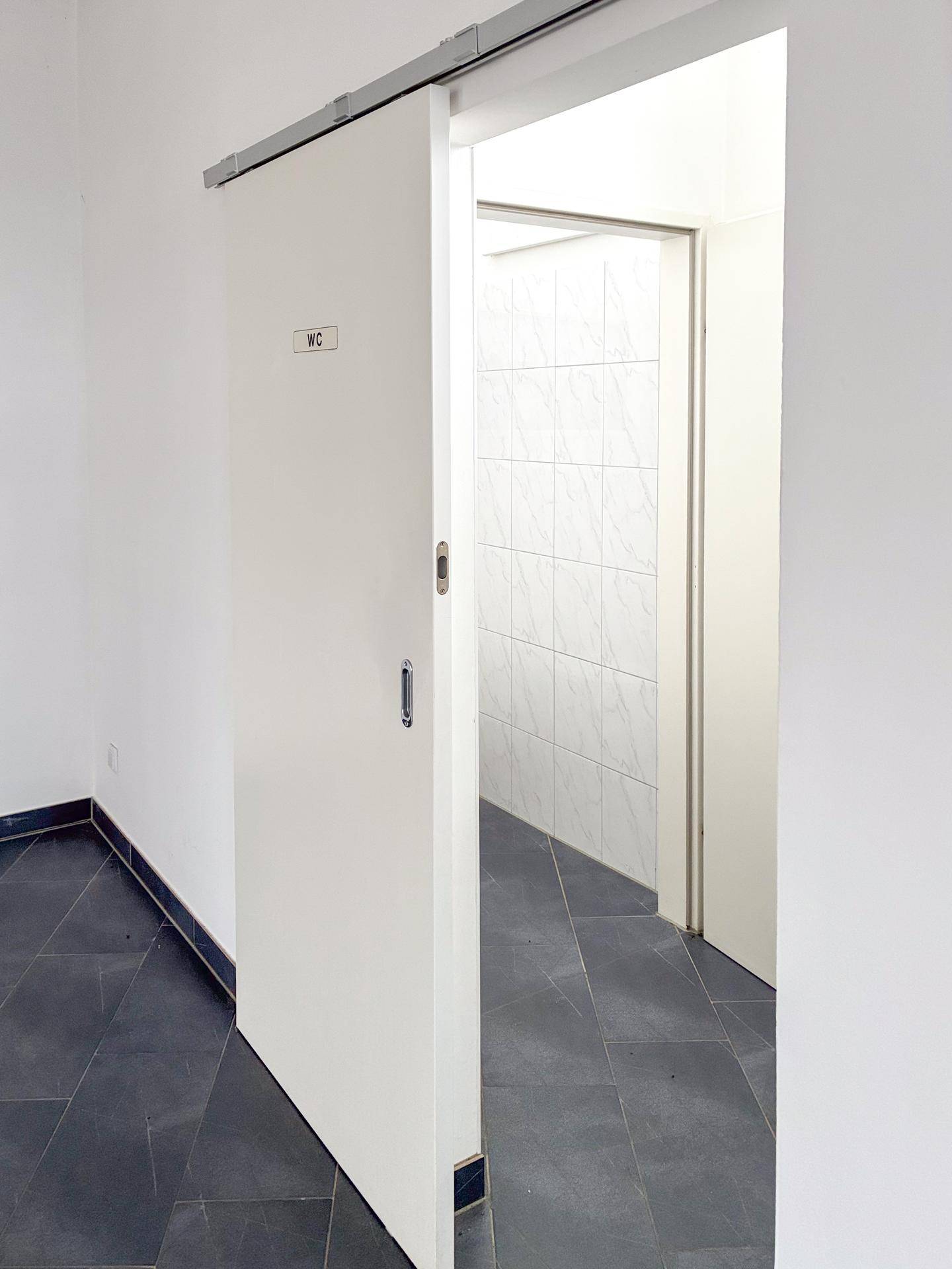 Eine Schiebetür mit der Aufschrift "WC" führt in einen sauber gefliesten Toilettenraum.