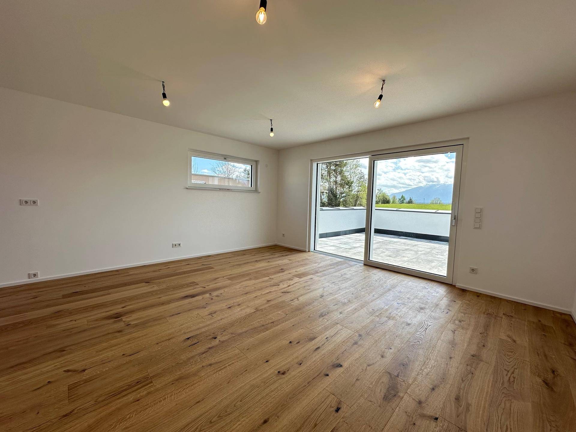 Heller, unmöblierter Raum mit Holzboden und großer Schiebetür, die zur Terrasse führt.