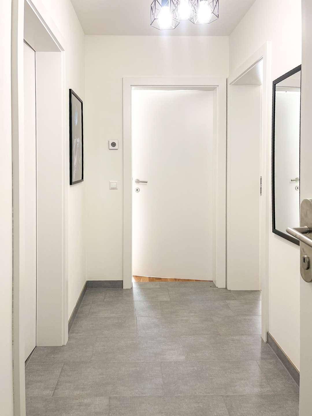 Heller Flur mit modernen grauen Fliesen und weißen Türen.