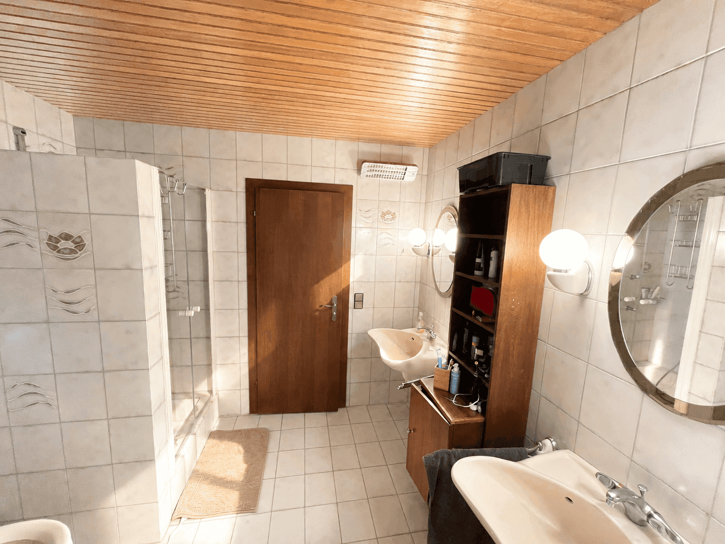 Funktionales Badezimmer mit hellen Fliesen, zwei Waschbecken und Duschkabine.