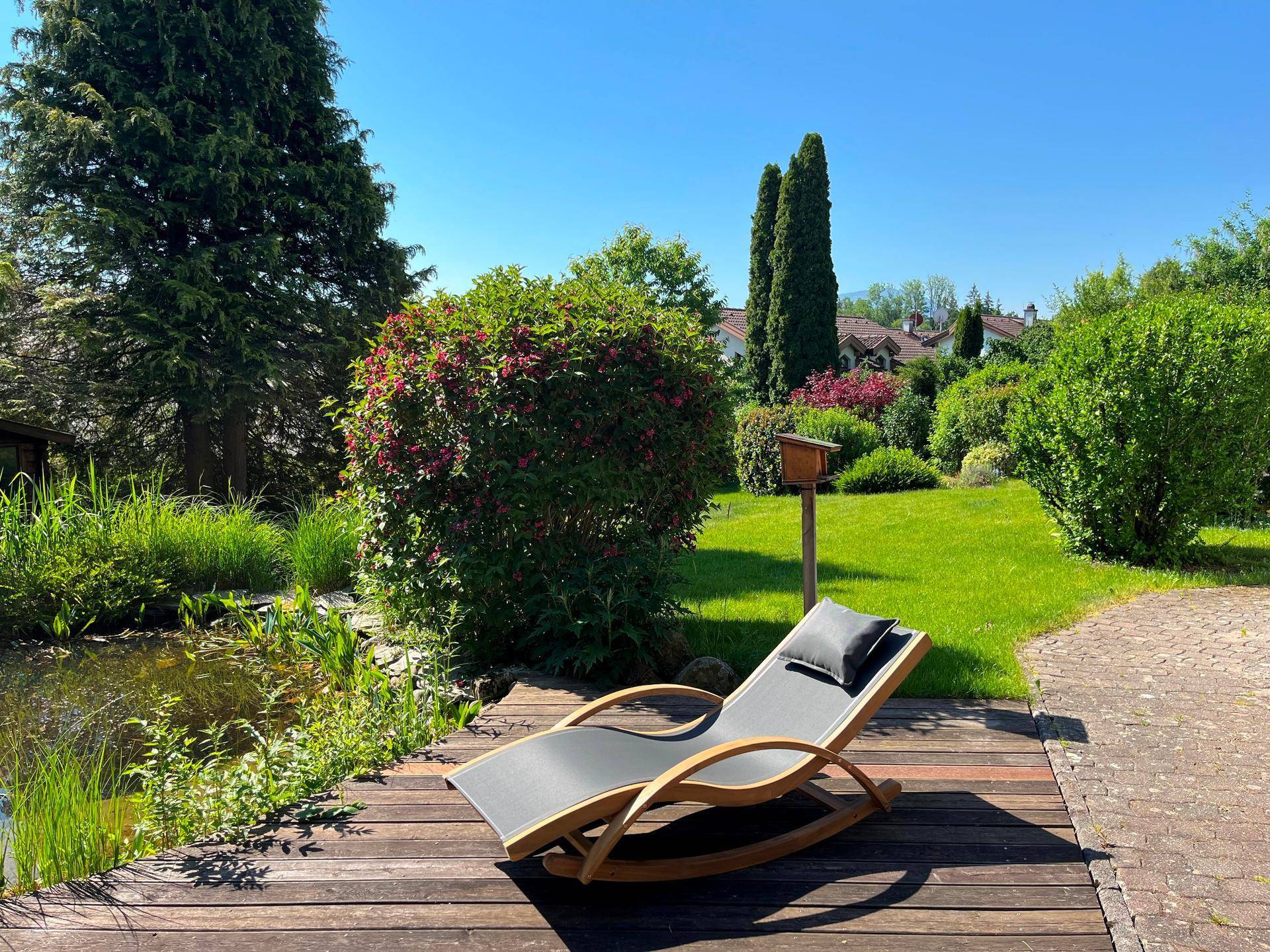 Sonniger Gartenbereich mit Holzterrasse und bequemer Liege zum Entspannen.